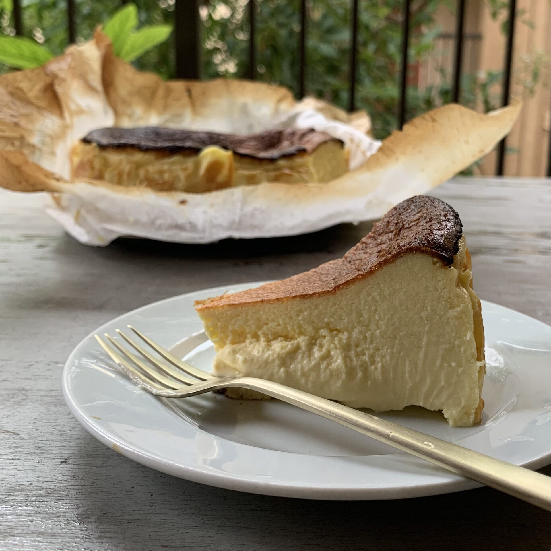 A slice of gluten free Basque cheesecake on a plate, with a whole cake in the background